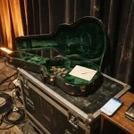 Open guitar case with plain coins and an envelope backstage, reflecting the Mr Pacho review