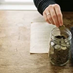Hand dropping coins into a jar beside a short terms page, reflecting the Rakebit review